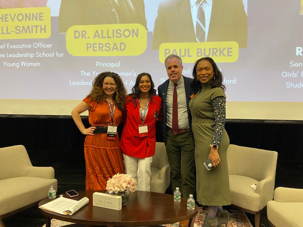Four speakers and panelists pose for photo on the auditorium stage
