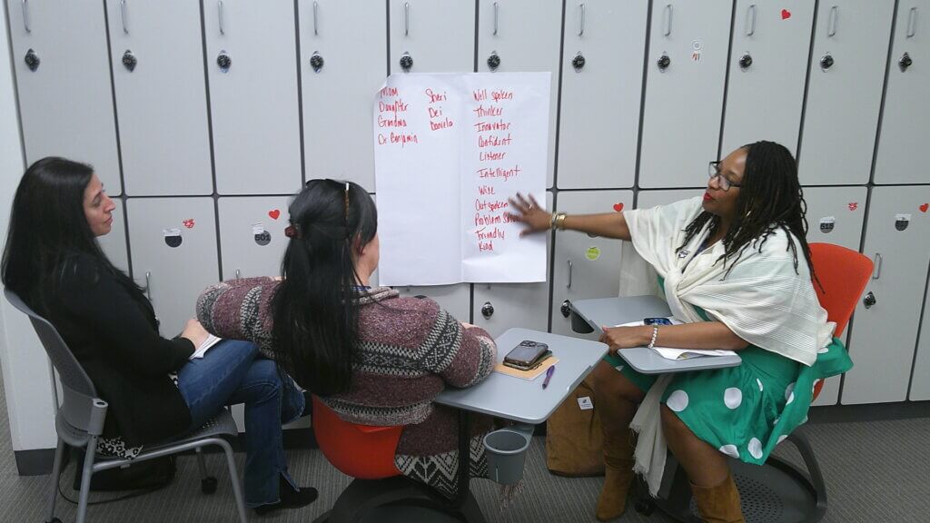 Three seated women point to a list on the wall of women leaders