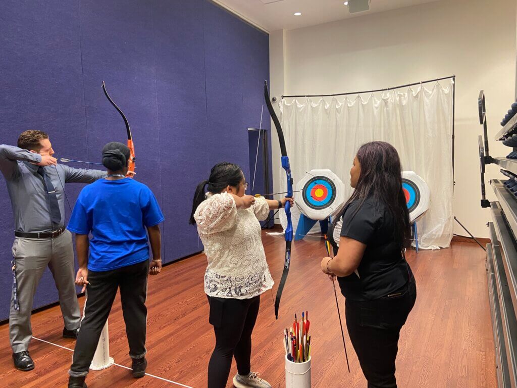 Two instructors and two adults position arrows and bows aimed at archery targets
