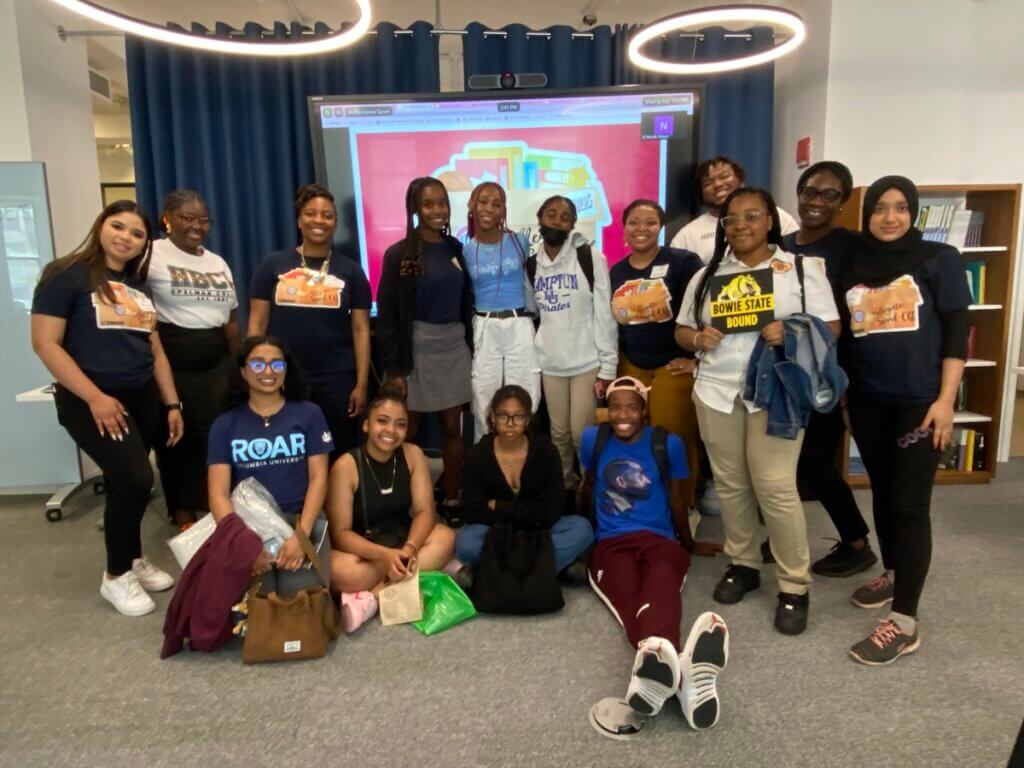 Group of students and alumni wearing college shirts pose for photo
