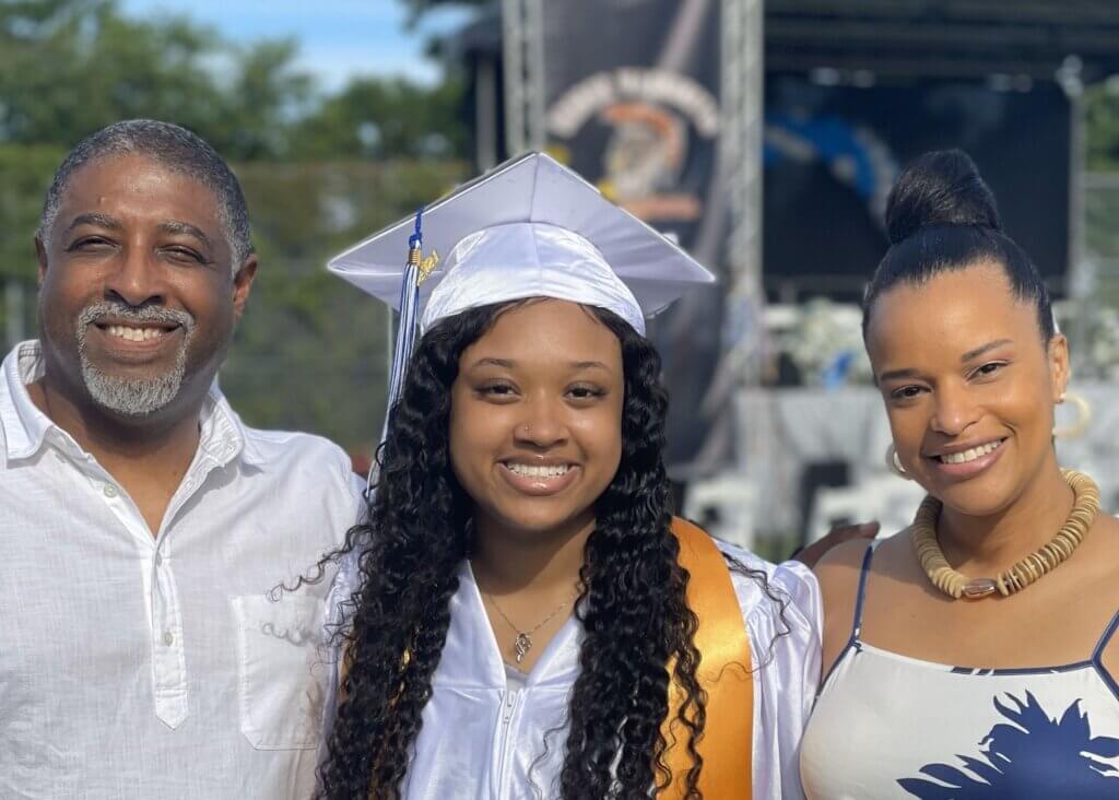 Young woman in a graduation cap and gown with her parents on either side of her