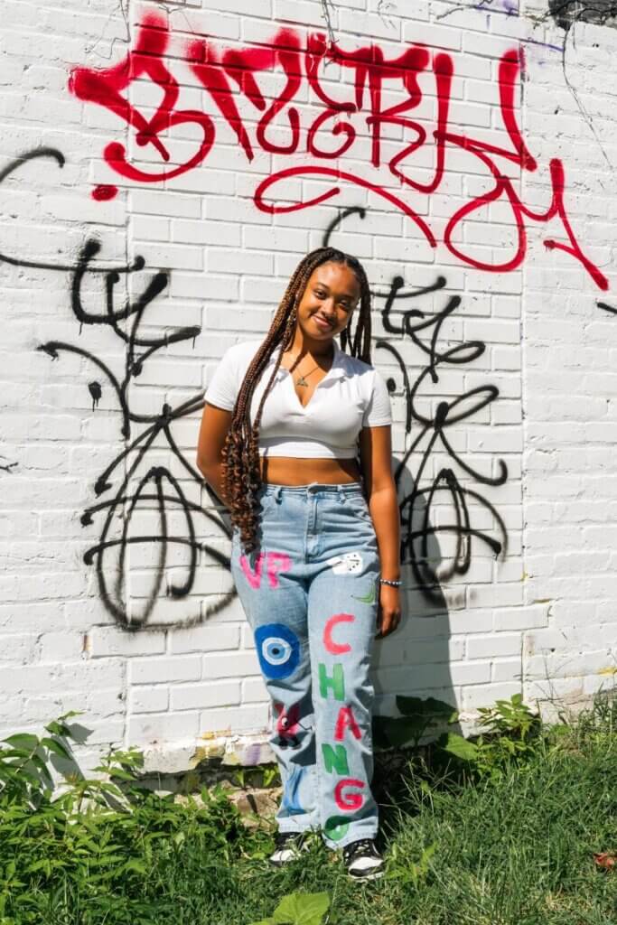 Young woman wears jeans with "Chango" drawn on one leg in colorful letters and "VP" drawn on the other