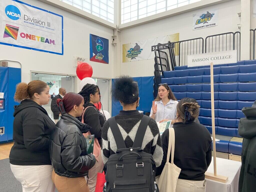 High school students visit a variety of college admissions tables inside a large gymnasium