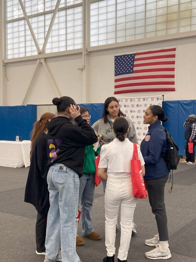 A director of college counseling speaks to a group of girls in the gym
