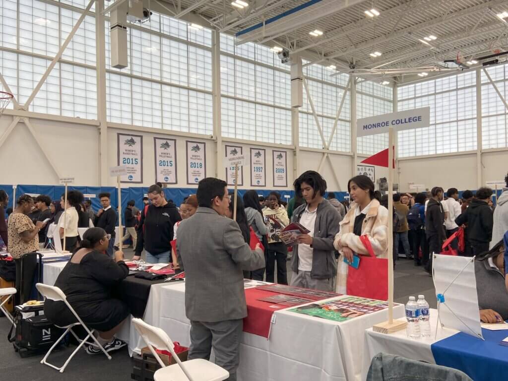 High school students visit a variety of college admissions tables inside a large gymnasium