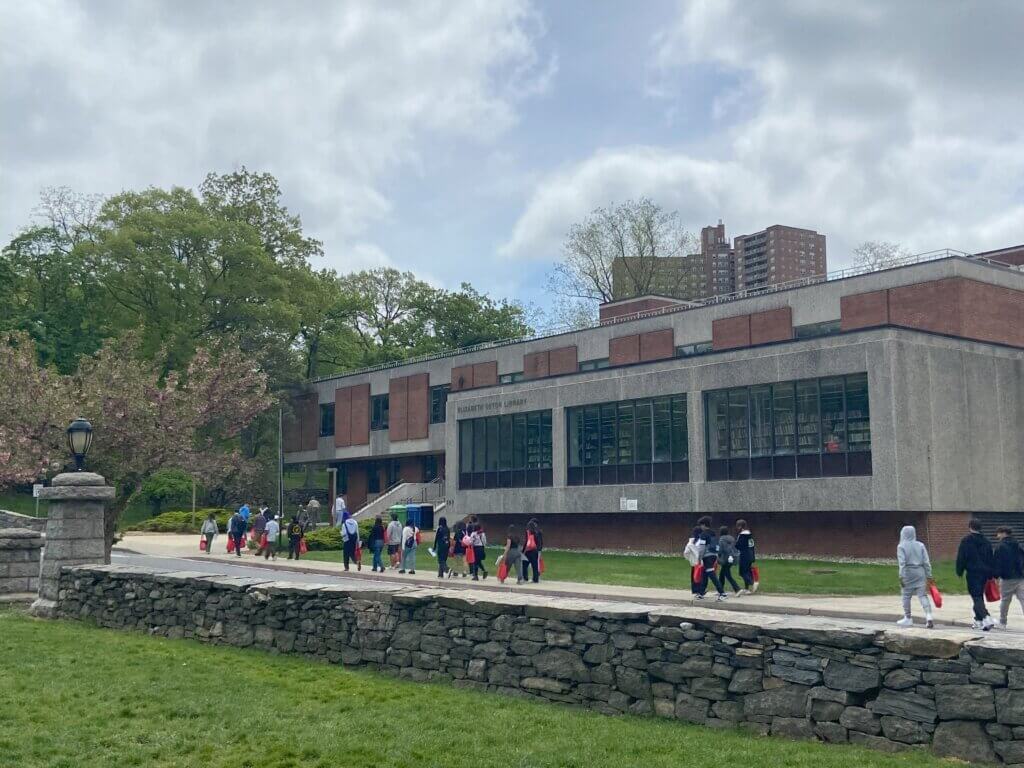 Students tour a college campus, with stone walls lining a green landscape with trees