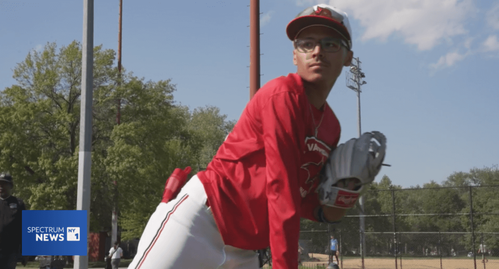 male student wearing red and white baseball uniform holds a pitchers glove on a baseball field