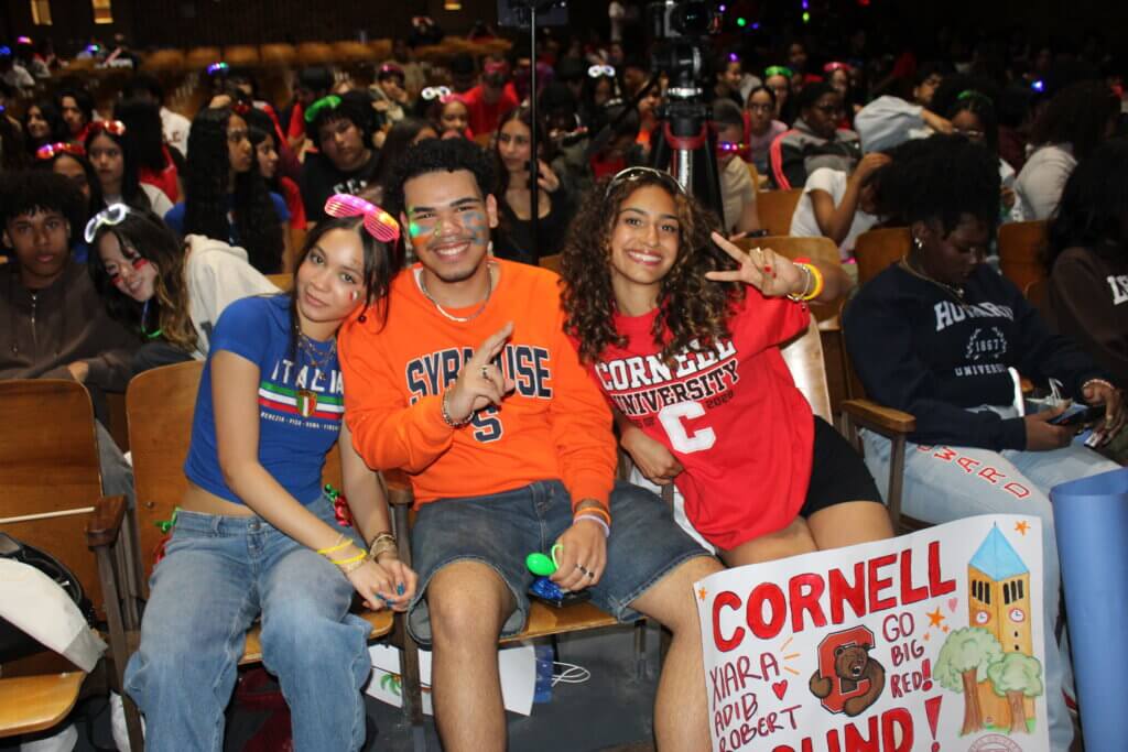 Students wearing college t-shirts smile and make peace signs