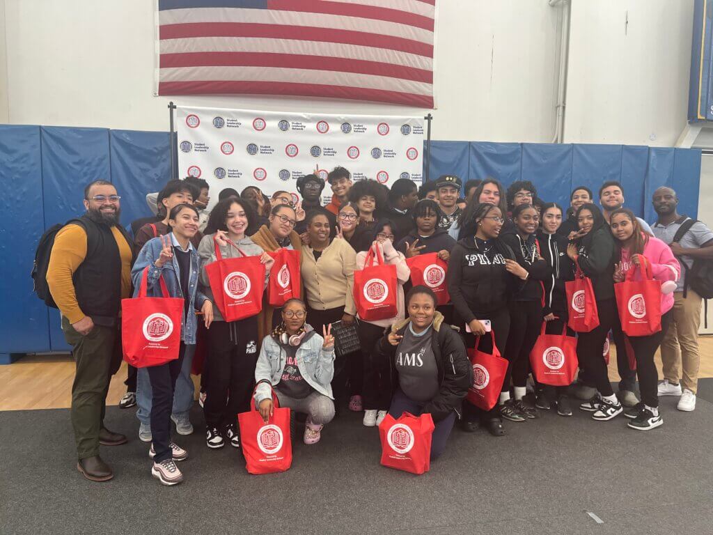 Eleventh grade students and their director of college counseling pose for photo, holding bright red CollegeBound Initiative tote bags