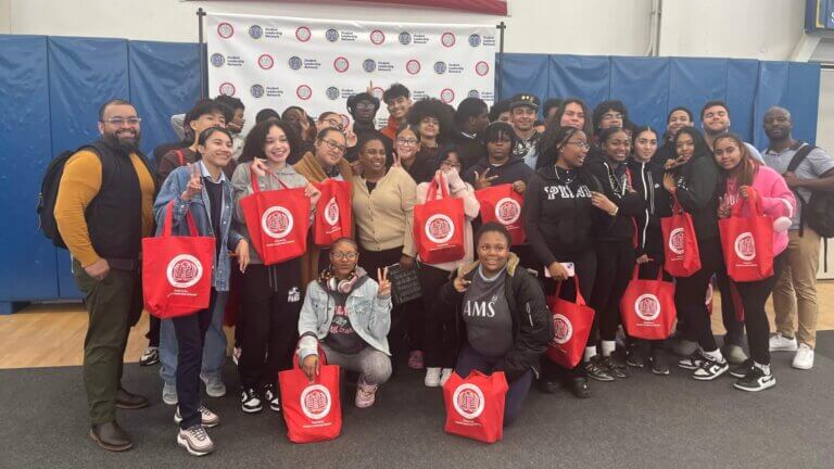 Eleventh grade students and their director of college counseling pose for photo, holding bright red CollegeBound Initiative tote bags