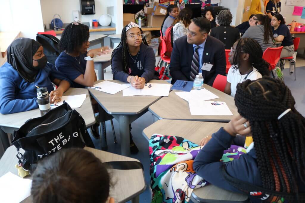 Adult volunteer is seated in circular formation with middle school students