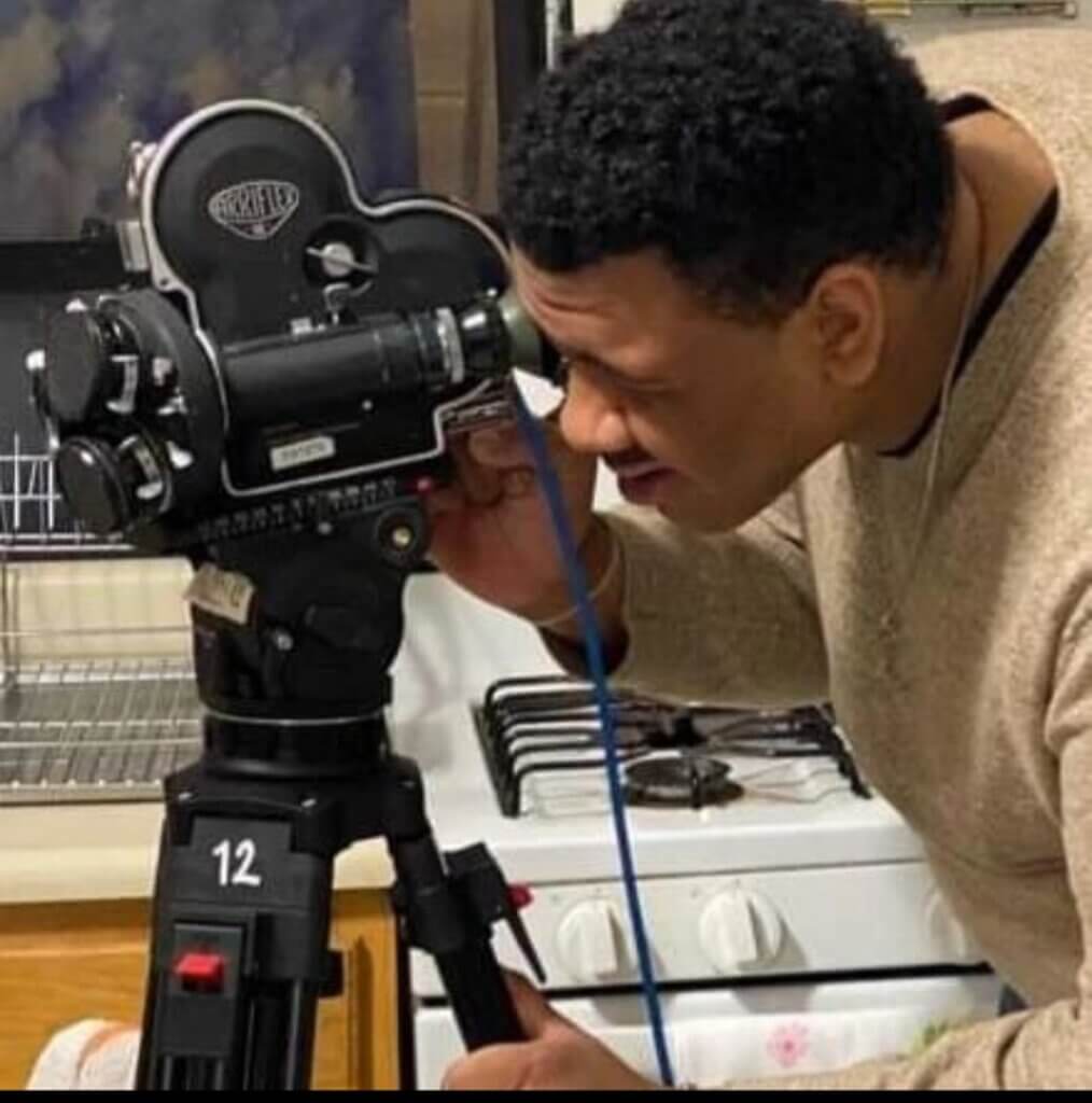 Young man is looking through viewfinder of a video camera on top of a tripod