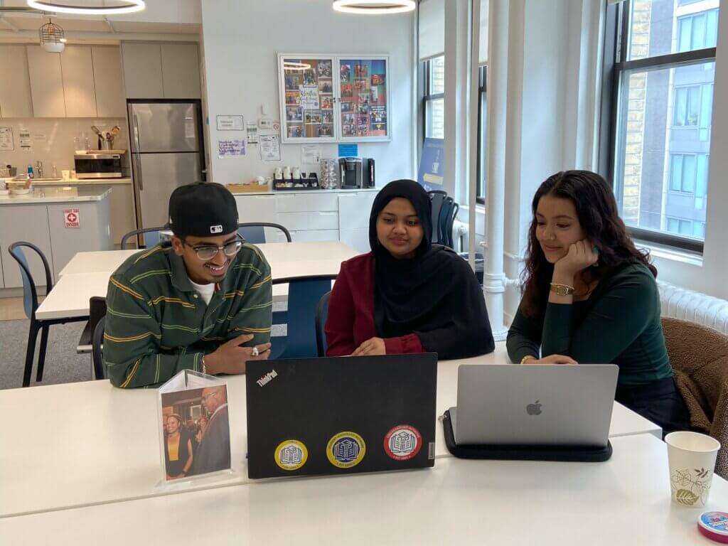 Three students gather around two laptops