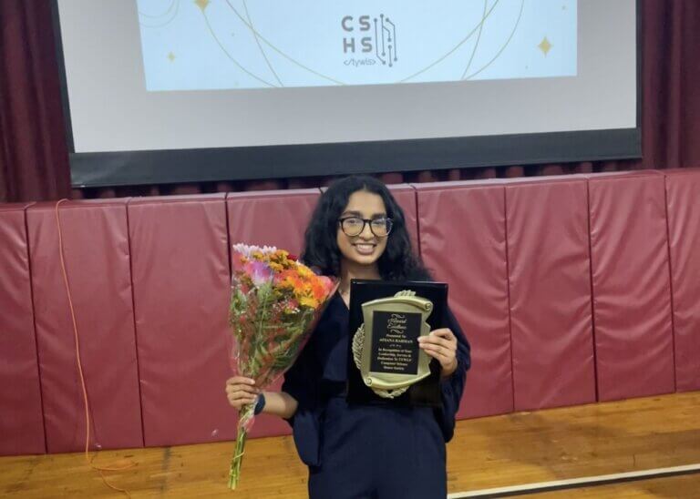 Young woman holds up an awards plaque and flowers at a computer science honors induction ceremony