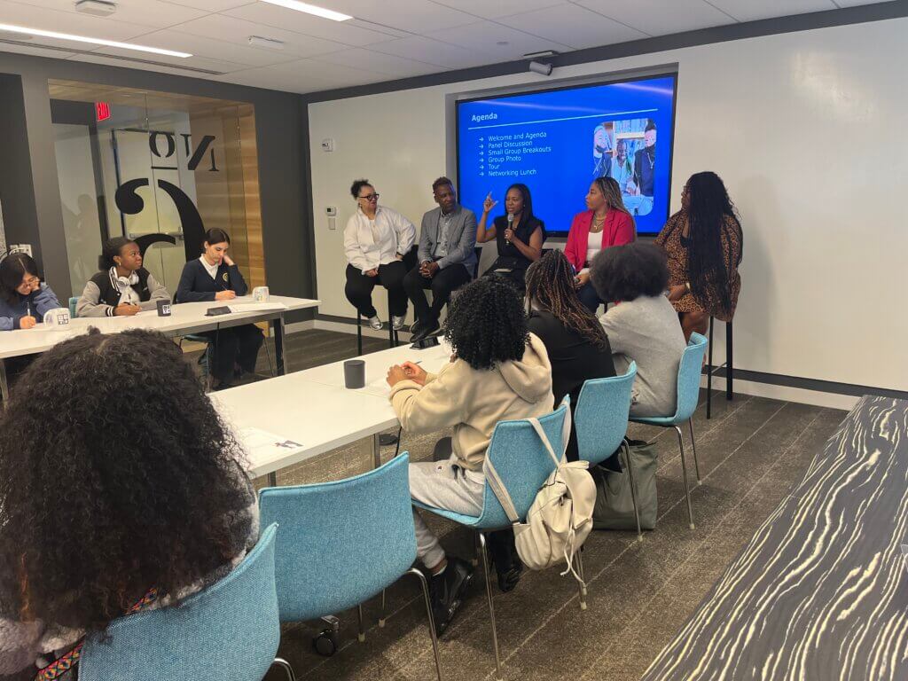 Five employees at BET who are people of color are seated at front of room with microphones, talking with students who are seated in the room