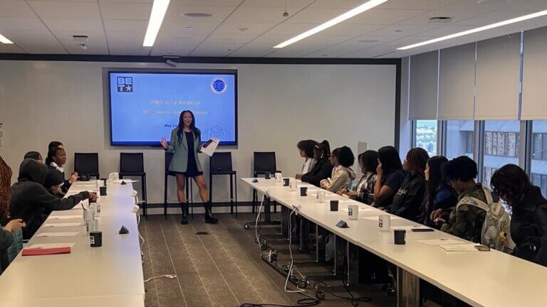 BET employee welcomes students at front of room, while students are seated at two long conference tables