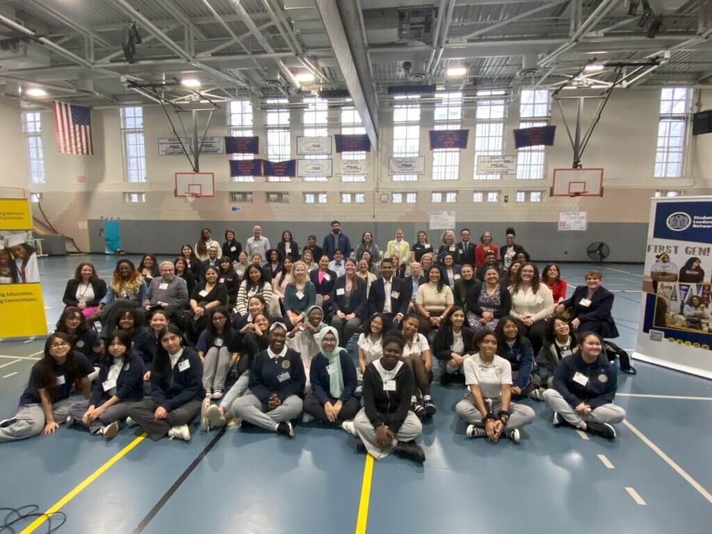 Large group of over 70 adult volunteers and students are seated in the gym for group photo