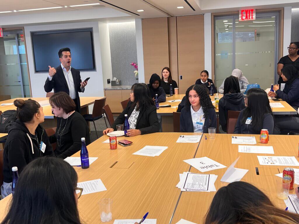 Bank employee stands in conference room, speaking to a group of students who are seated