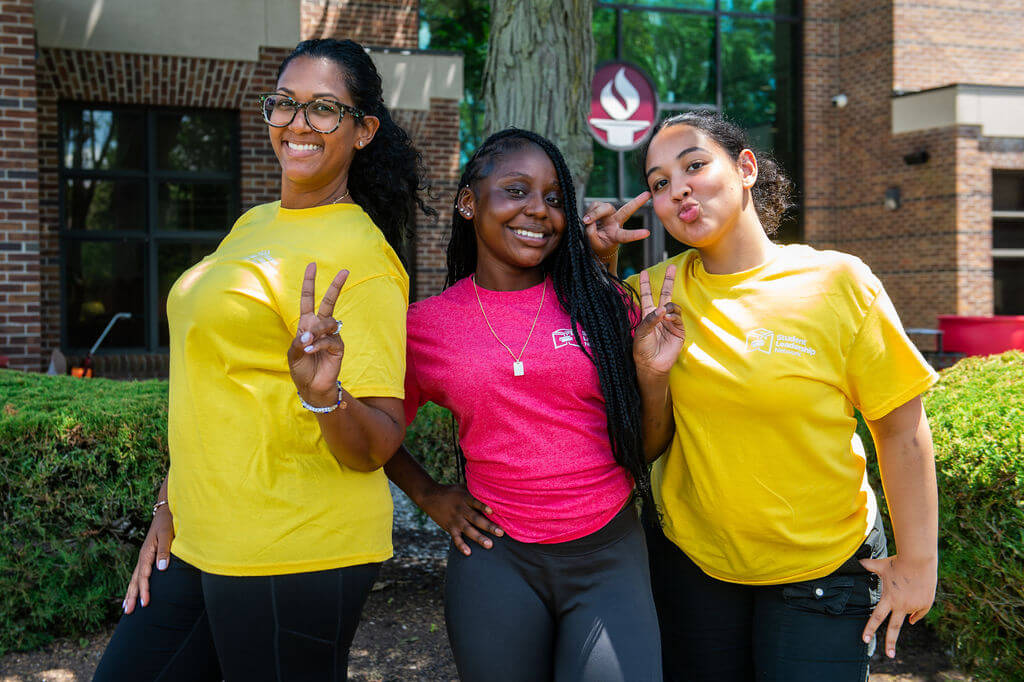 A counselor and two of her students pose for a photo outdoors with hands in peace signs