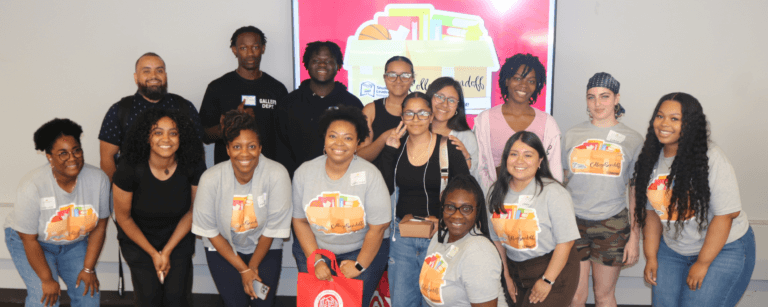 Students, alumni, and staff stand in two rows to pose for a photo