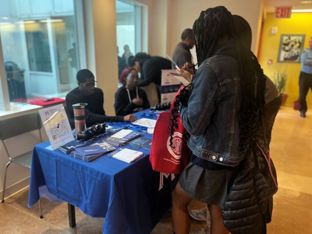Students visit a college table and talk with Mercy University staff.