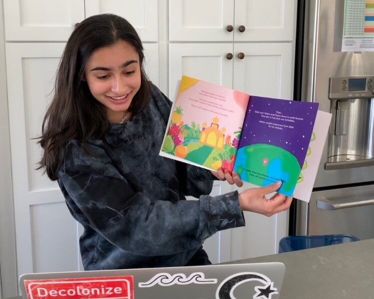 Teenage girl holds up book and reads to a virtual buddy on her laptop screen