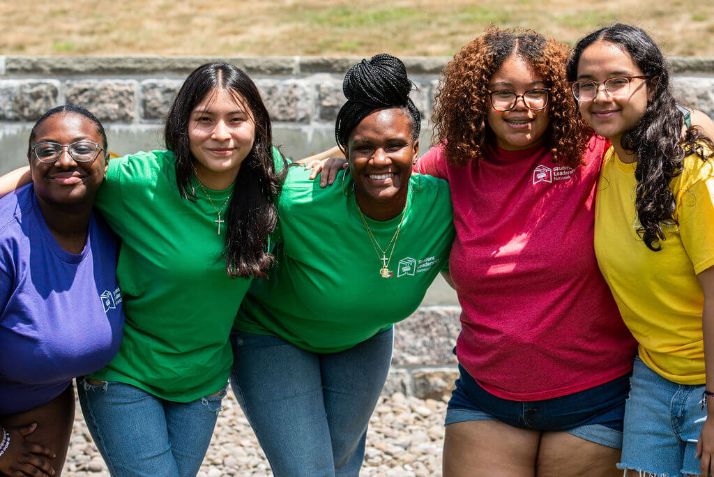 Adult college counselor with four students lean in with their arms around each other's shoulders