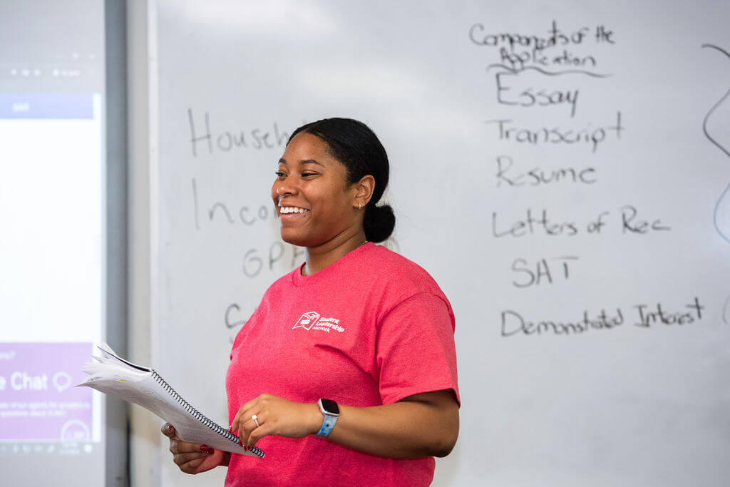 Woman smiles in front of a board that lists out components of a college application