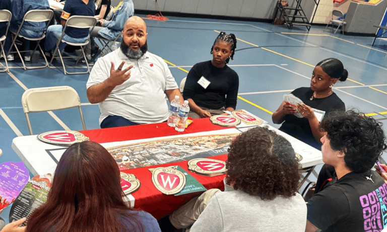 College representative is seated with students around a table with college materials