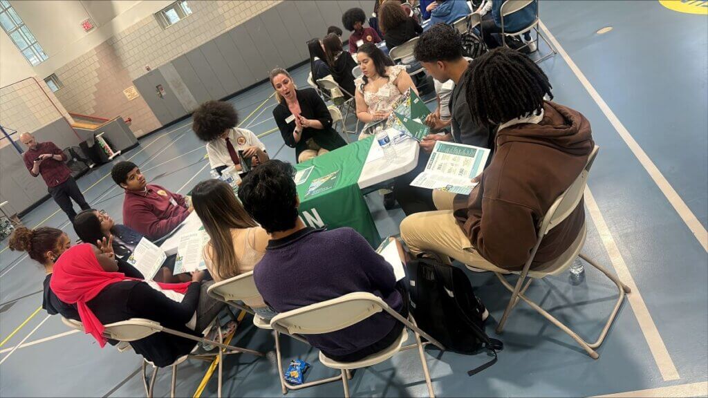 College representative is seated with students around a table with college materials