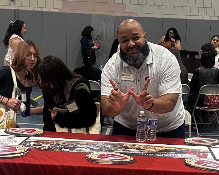College representative holds fingers in a "W" shape by the University of Wisconsin-Madison table