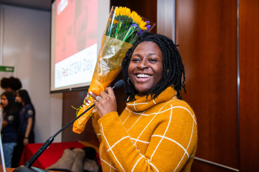 Staff member Folasade speaks into microphone, holding up a bouquet of flowers