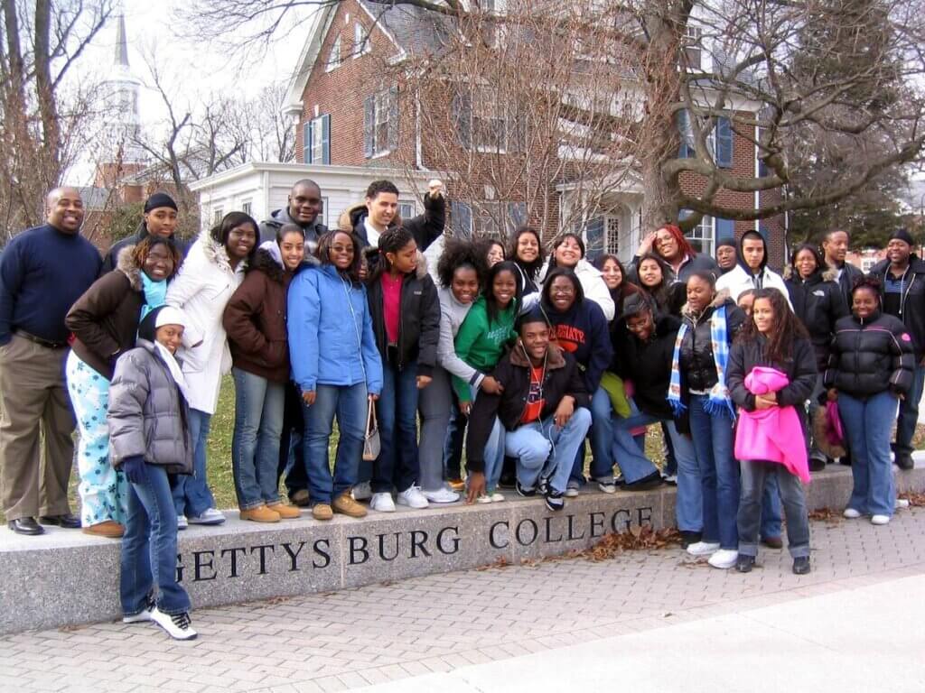 Students wearing winter clothes pose with parents and guardians in front of Gettysburg College sign