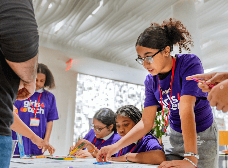Four girls in purple Girls4Tech t-shirts gather around a table for cybersecurity activity