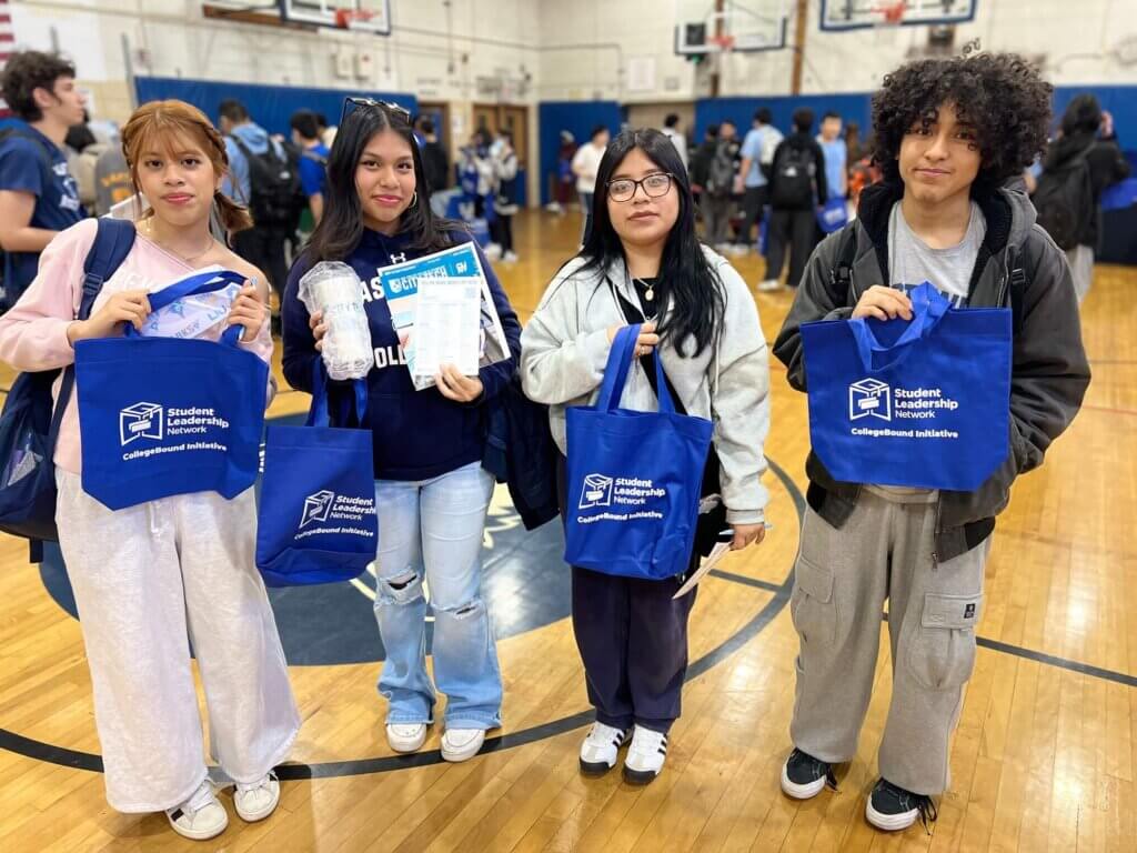 Four students hold up Student Leadership Network bags and college brochures