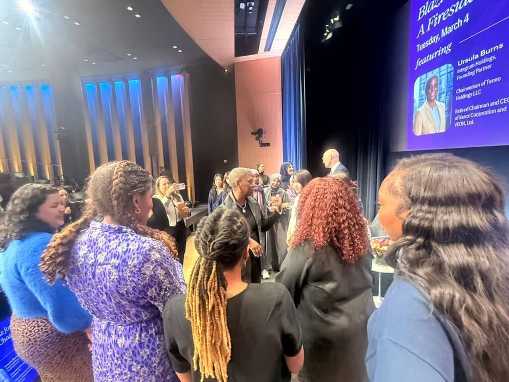 Students gather around Ursula Burns on a stage