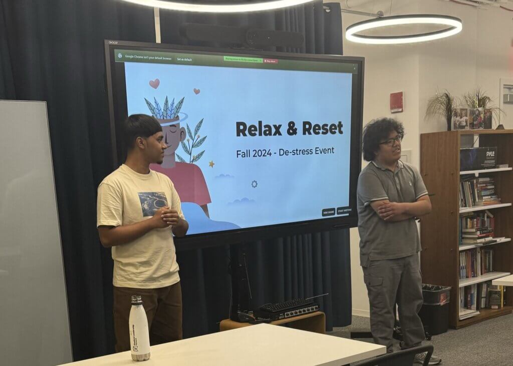 Two male alumni stand in front of their presentation for college students