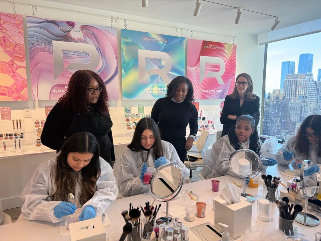 Students wearing lab coats mix ingredients for lip glosses.
