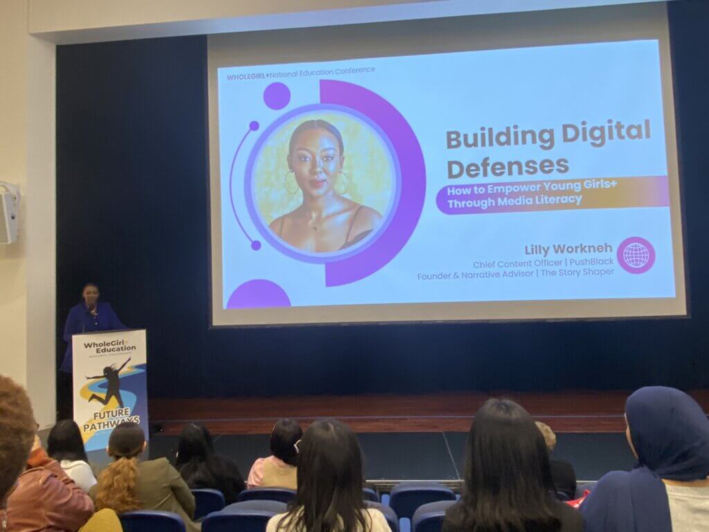 LIlly Workneh stands behind podium with her presentation on a slide on stage