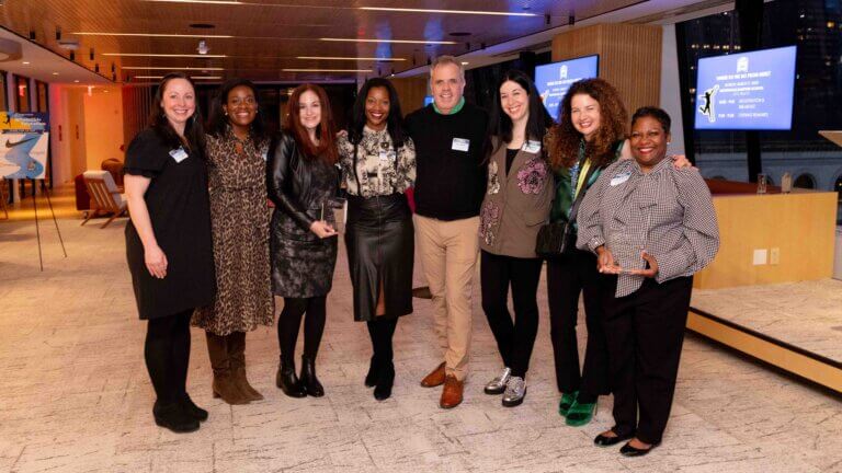 Group of educators in festive attire pose for photo, two adults are holding up crystal awards