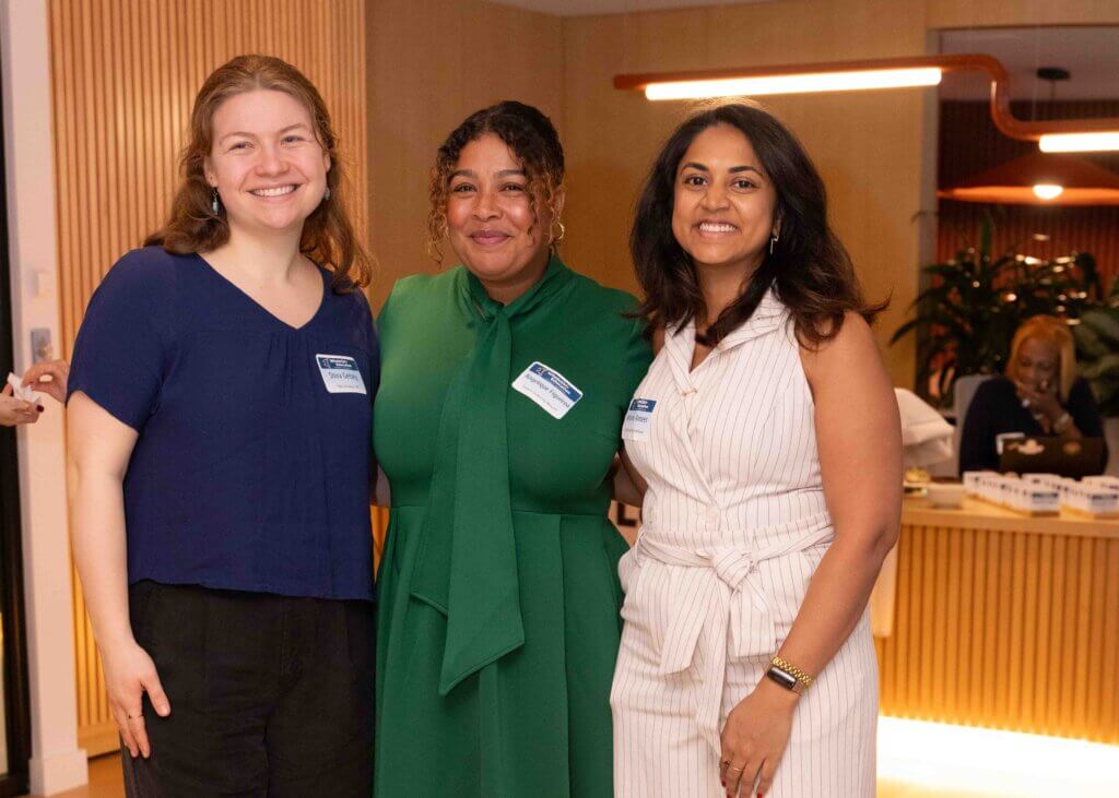 Three women in festive attire smile confidently at camera