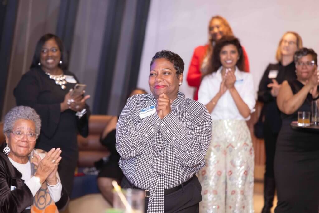 Dr. Charcia Nichols clasps hands together with a smile with people clapping their hands at her award announcement