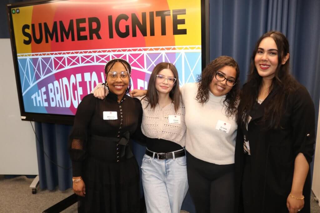 Four young women pose in front of panelist screen