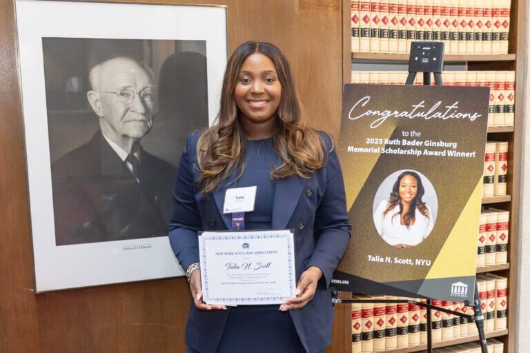 Talia Scott holds up a certificate in front of the NYU Law school library