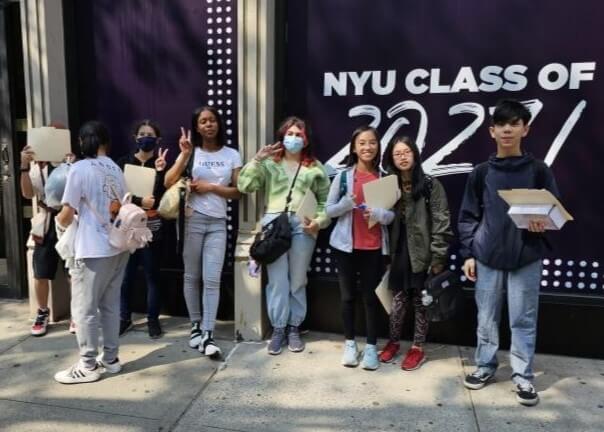 Group of students stand outside in front of a sign reading NYU Class of 2027