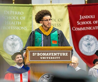 A graduate in cap and gown serves as Commencement Speaker at a podium labeled St. Bonaventure University