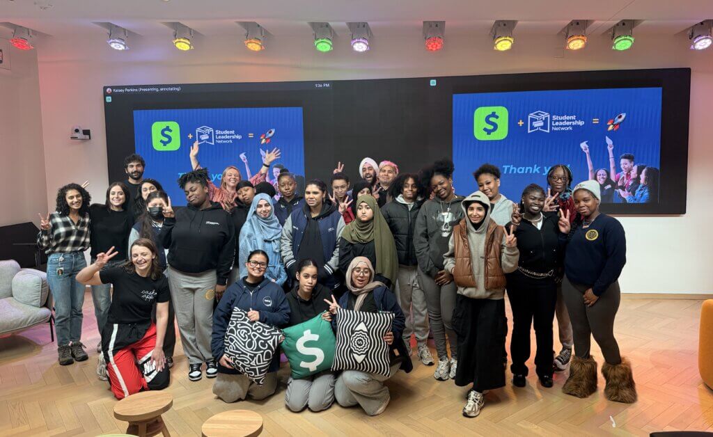 A group of people pose for a photo in front of large screens displaying Student Leadership Network and Thank you graphics in a modern, well-lit room.