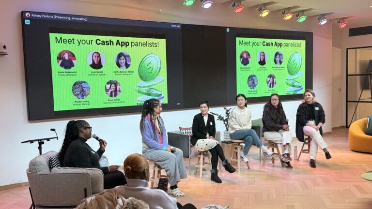 A panel of six women sit on stools in front of an audience, speaking at a Cash App event with an introduction slide displayed on screens behind them.