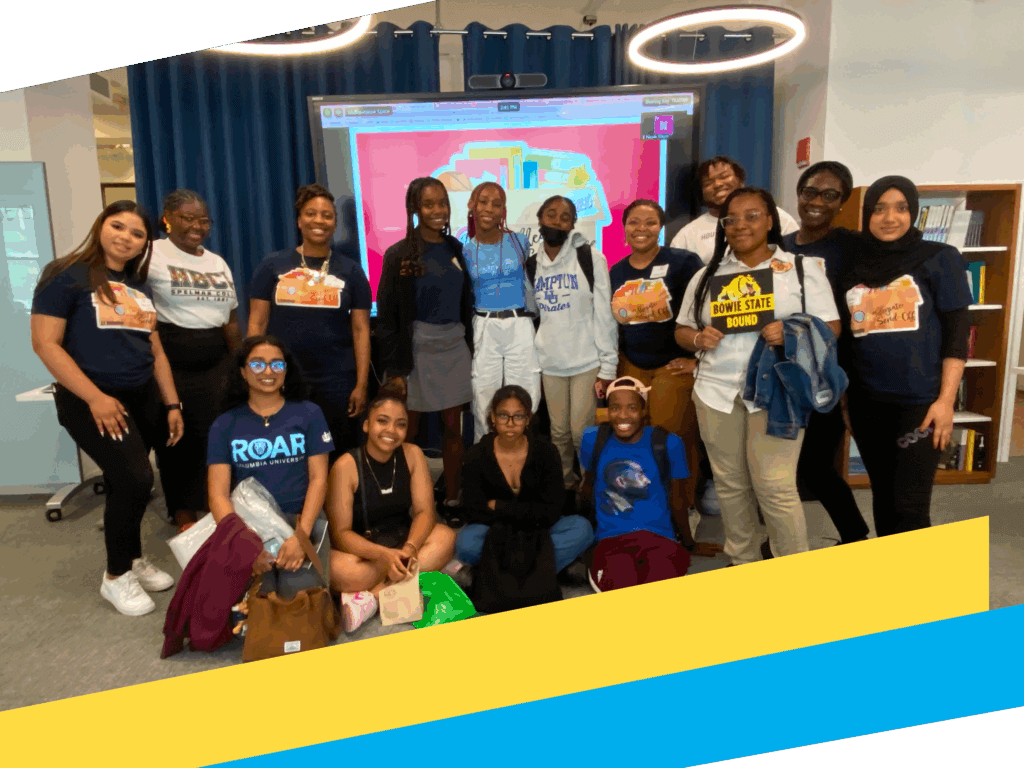 A group of sixteen young women pose together in a library or classroom space, standing and kneeling in front of a colorful digital display highlighting college persistence and graduation support.