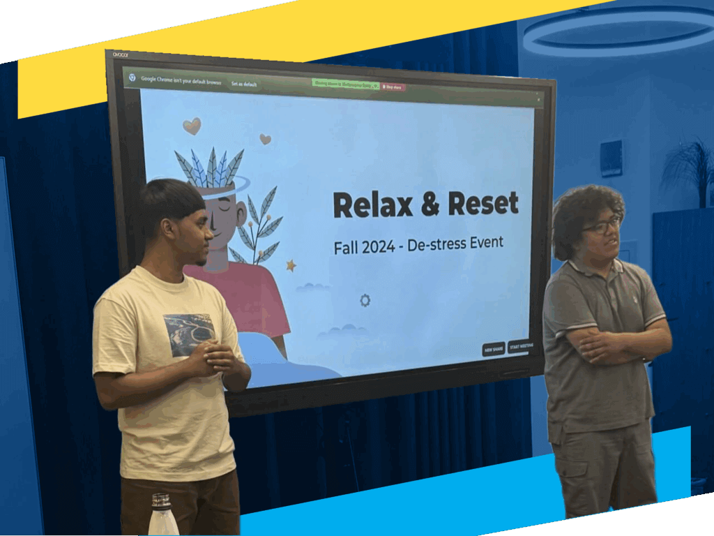 Two people stand in front of a screen displaying a presentation titled Relax & Reset: Fall 2024 - De-stress Event, highlighting college persistence and graduation support, in a room with blue curtains and a circular ceiling light.
